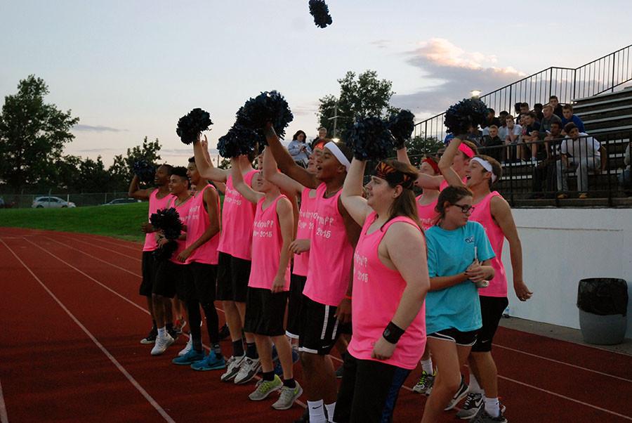 Guys on the powder puff cheer squad cheer on the powder puff football players during the initial kickoff to start the game.