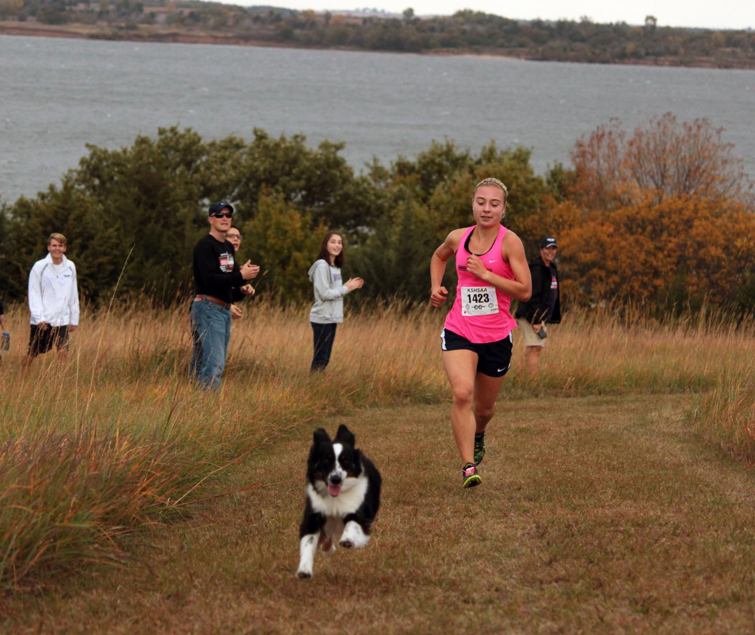 Junior Clara Mayfield rounds the corner at cross country regionals. Mayfield was joined by a loose dog, Della, for a few meters before returning to her owner.