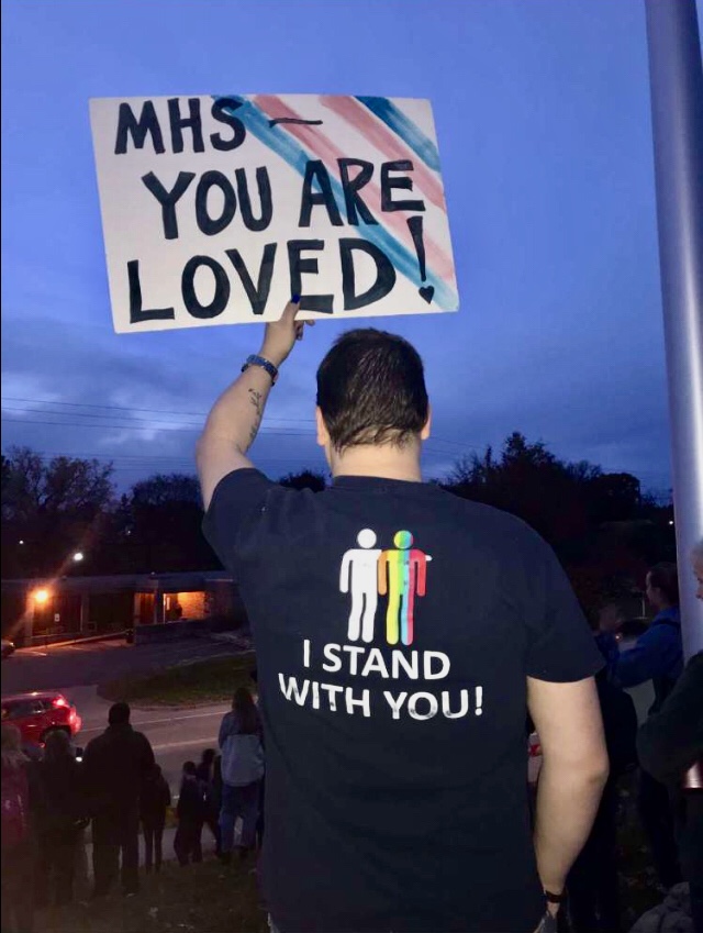 Gay+Straight+Alliance+sponsor+and+Environmental+Science+teacher+Clancey+Livingston+holds+a+sign+of+support+while+he+looks+upon+the+student+counter-protestors+--+lead+by+Student+Body+President%2C+senior+Parker+Wilson+--+as+Westboro+Baptist+Church+protests+GSA+and+the+LBGTQ%2B+community+of+Manhattan+High.+The+protests+took+place+just+outside+of+MHS+7%3A10+to+7%3A40+the+morning+of+Nov.1++