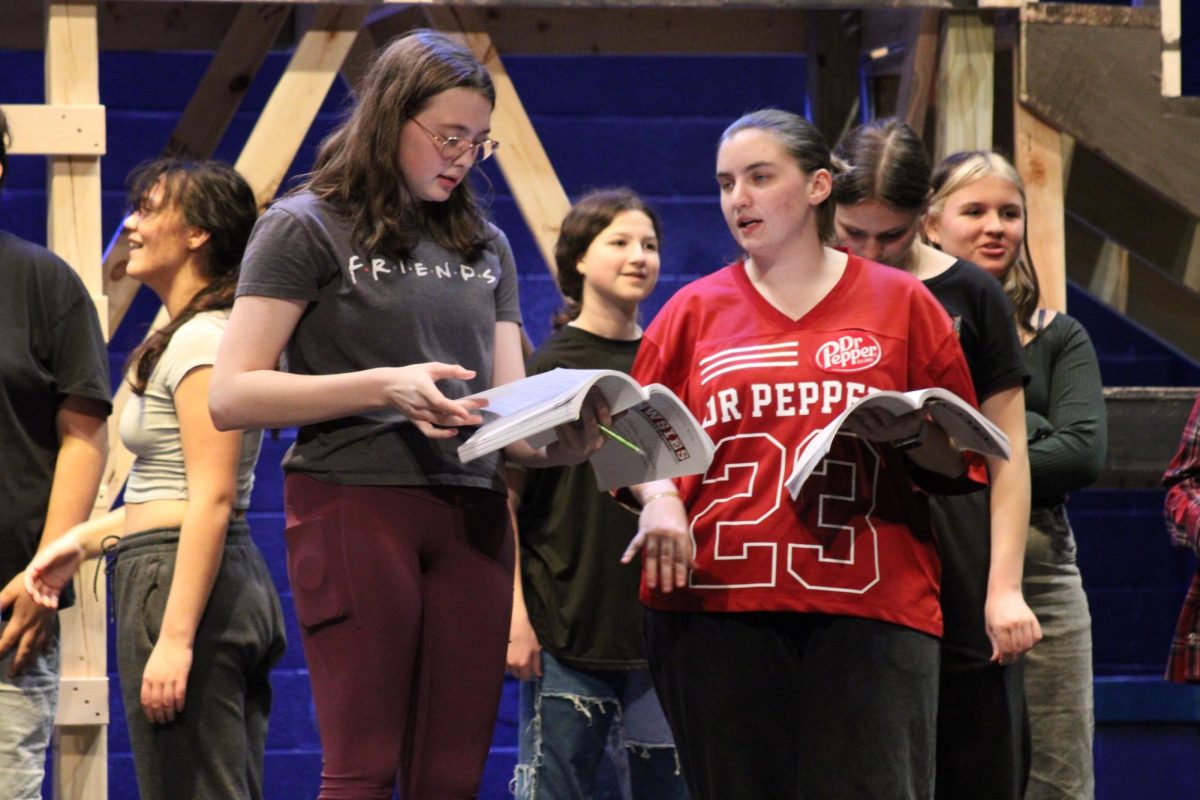 Notes in rehearsal. Junior Ella Chase and senior Leah Herring talk about their scripts as the musical rehearsal moves along. The practice these students are in are for the MHS Spring Musical Newsies, that is going to be performed on Mar. 6,7 and 8, 2026. 