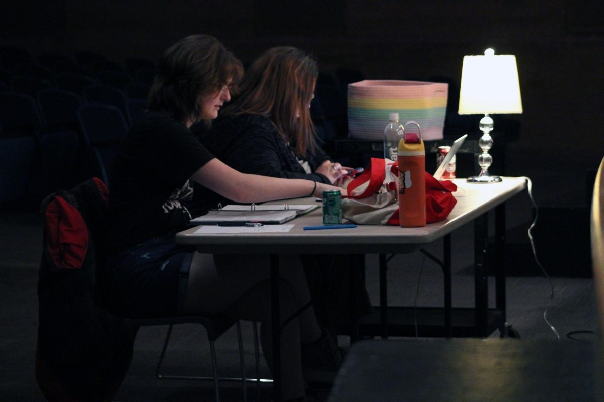 Lamp light. Junior Brynna Hight sits with the Drama teacher, Virginia Pape, and goes through the main script and scenes with the actors on the lit stage during the tech day, which is when the actors and cast members for on set, costumes, cues, and more. The play that the Manhattan High School Theatre Department is putting on is called Proof. The tech day was on Apr. 26.