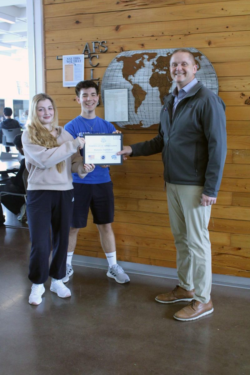 Standing and smiling. Exchange students, Khadija Ahmad and Marc Buerger hand over an award to the principal of Manhattan High School, Michael Dorst. The award is from the AFS program that is an award of recognition and appreciation for having two funded exchange students roam the school.