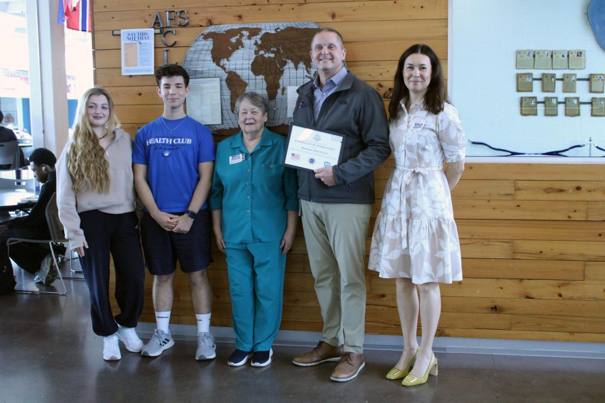 Group photo. Visitors from the AFS program take a picture with the two of the exchange students who are being supported and funded and with the Manhattan High School principal, Michael Dorst, to give him an award of appreciation for hosting these two students and the others as well. The award was given on Apr. 27, during the period of first lunch and 5th hour. 