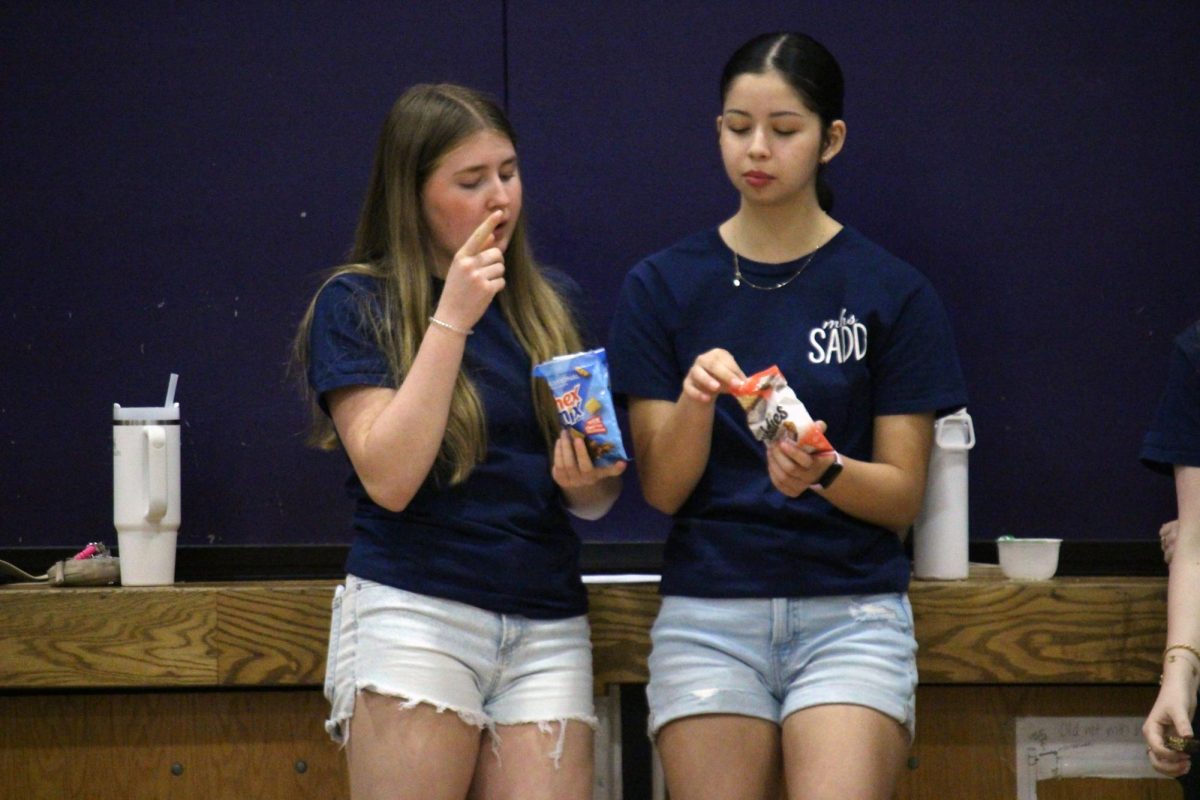 Snack break. Freshman Addi Hanschu and freshman Nicole Carranco chomp down on some snacks before the next herd of middle schoolers run into the Anthony Middle School gym for PE class. These two are a part of the club SADD, or Students Against Destructive Decisions, which is a club where these students travel to other schools and teach younger kids about bullying and dangers of addictions, such as with alcohol or substances. The visit to AMS was on Mar. 31.