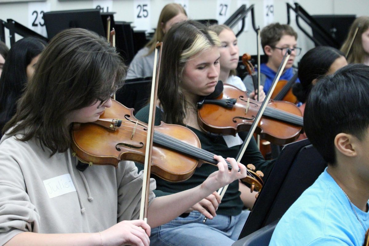 Strings galore! Freshman Juliet Parish and Freshman Eva Tortella cite read next to the Anthony Middle Schoolers while they visit from Manhattan High School to encourage these young musicians to keep on plucking in high school. The MHS Symphonic Orchestra visited Anthony Middle School on Mar. 31, during the school day.